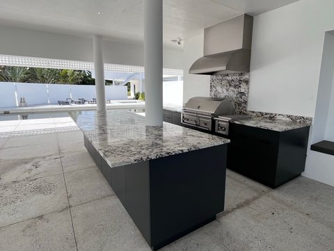 Covered outdoor kitchen with a separate dark island, built-in grill and overhead hood beside a pool.